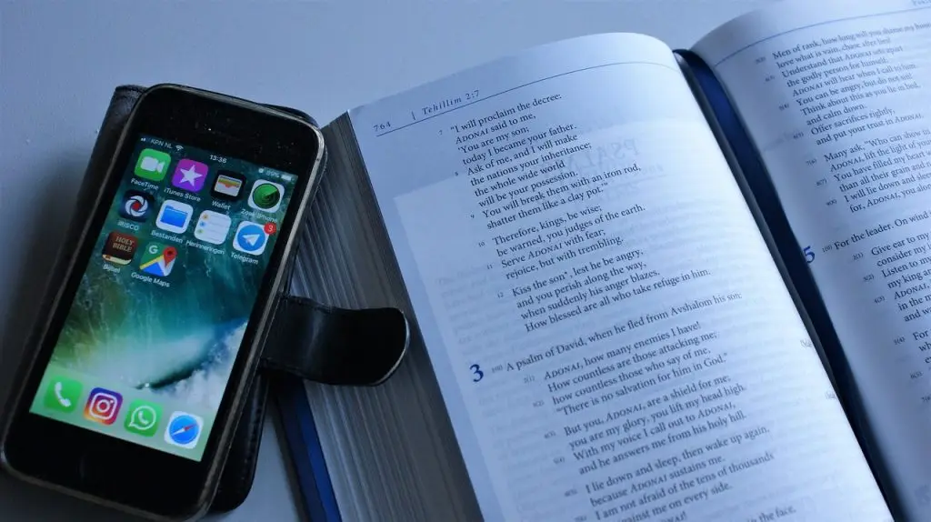 Open bible and smartphone showing apps on screen.