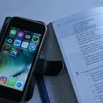 Open bible and smartphone showing apps on screen.