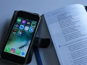 Open bible and smartphone showing apps on screen.