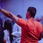 A man worships in a church holding a Bible among a congregation of diverse people.