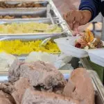 A person serves a variety of foods from a buffet station onto their plate.